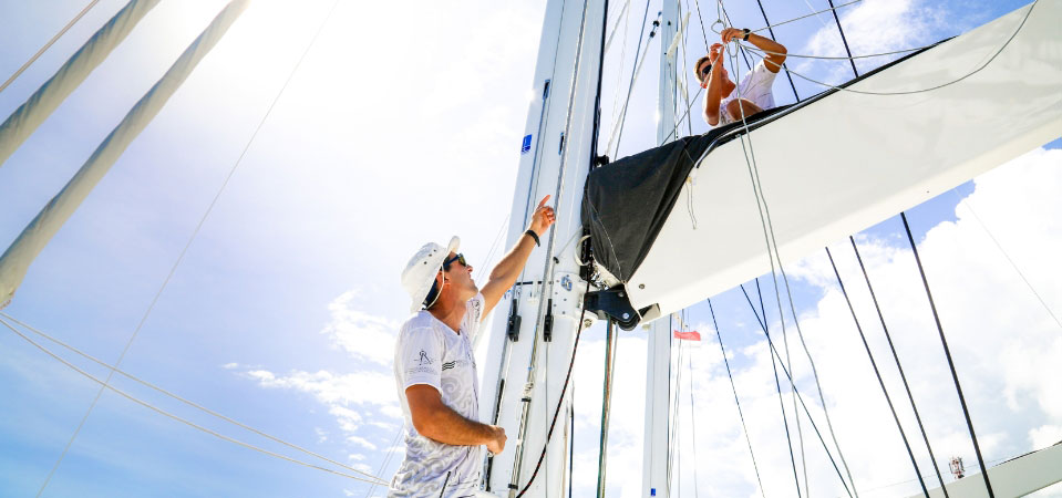 Crew member teaching a yachting apprentice about hoisting sails
